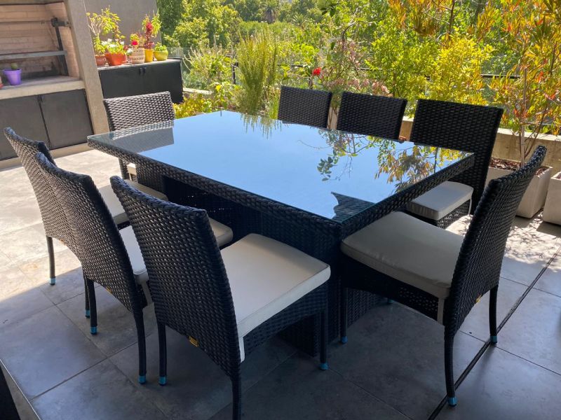 Conjunto de comedor de exterior MARYLAND en color Vintage Black, compuesto por una mesa rectangular con cubierta de vidrio y ocho sillas de ratán sintético con almohadones claros. Diseño elegante y resistente, ideal para terrazas y jardines.
